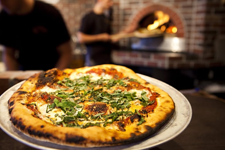 Workers preparing a margarita pizza from a wood fired brick oven